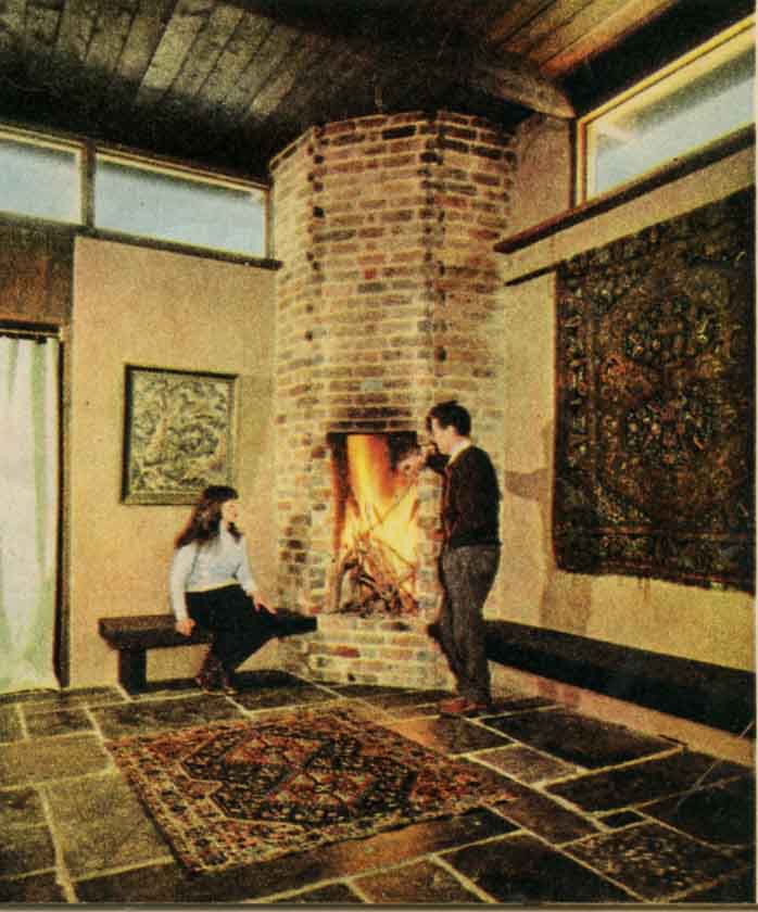 BESIDE THE UNUSUAL vertical fireplace in one corner of the central 'courtyard' room are the designer and his wife, Margot. Mr Knox says the fireplace was purely an experiment, but with ample firewood available in the surrounding bushland, he's proved it a 'roaring' success. It takes massive 4ft logs.